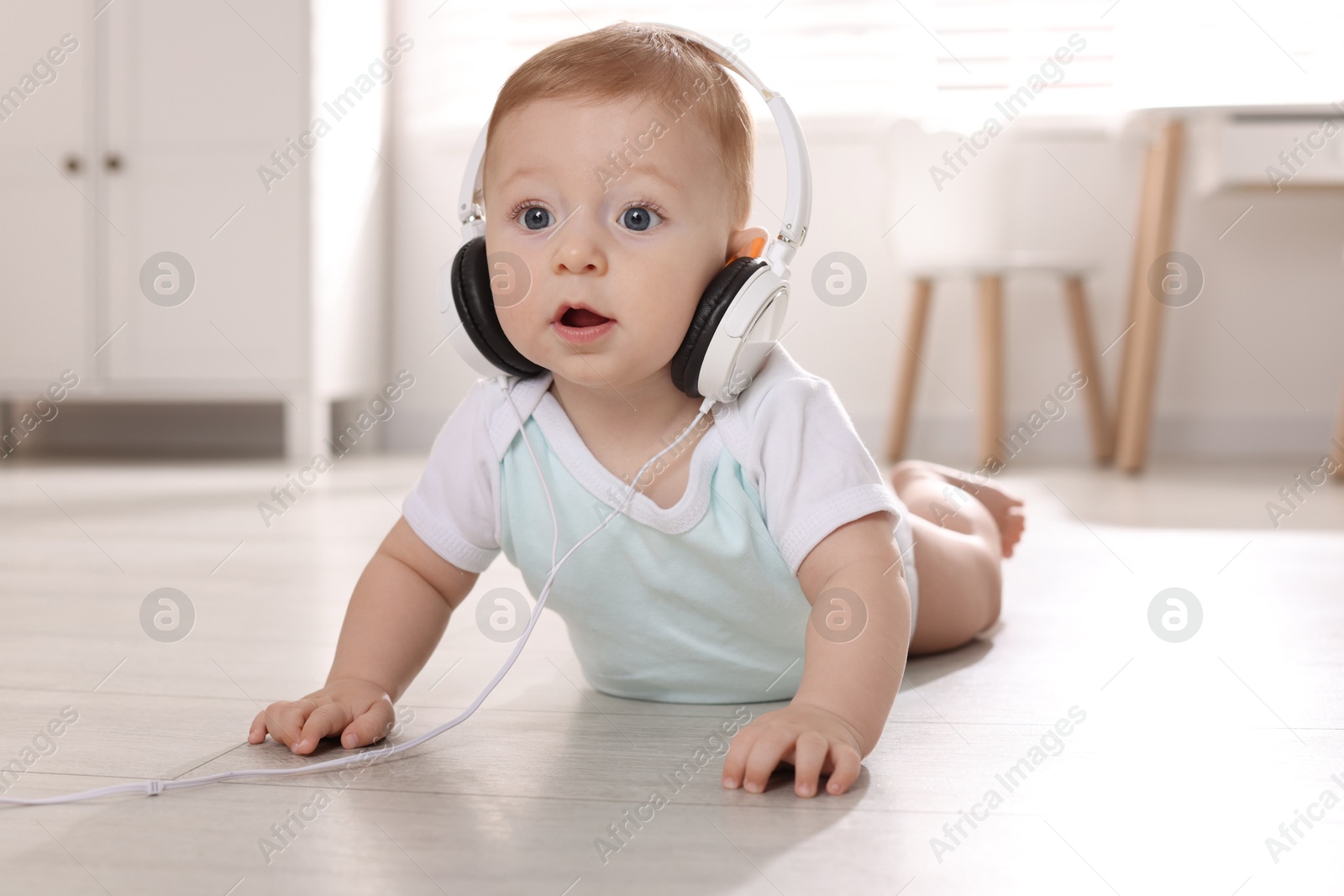 Photo of Cute little baby with headphones on floor at home