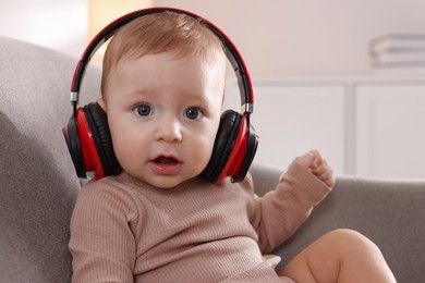 Cute little baby with headphones on sofa at home