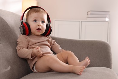 Cute little baby with headphones on sofa at home, space for text