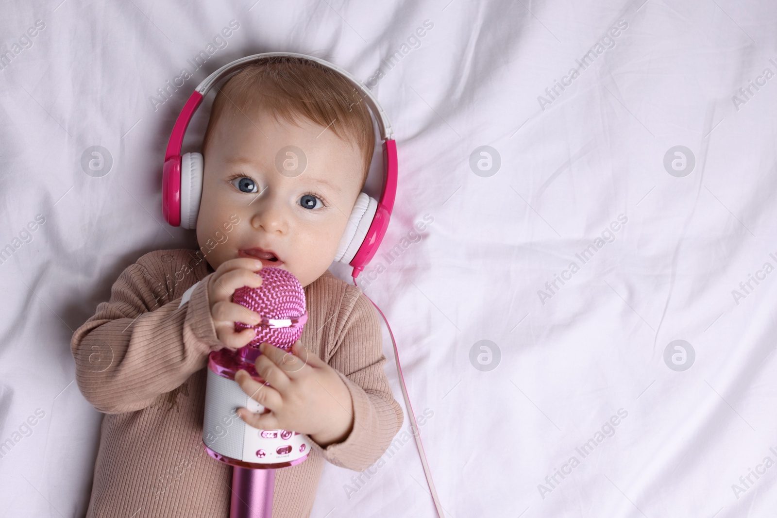 Photo of Cute little baby with headphones and microphone lying on bed, top view