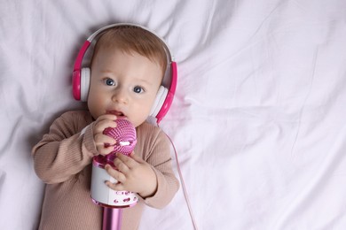 Cute little baby with headphones and microphone lying on bed, top view