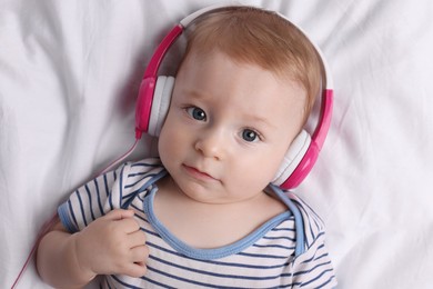 Photo of Cute little baby with headphones lying on bed, top view