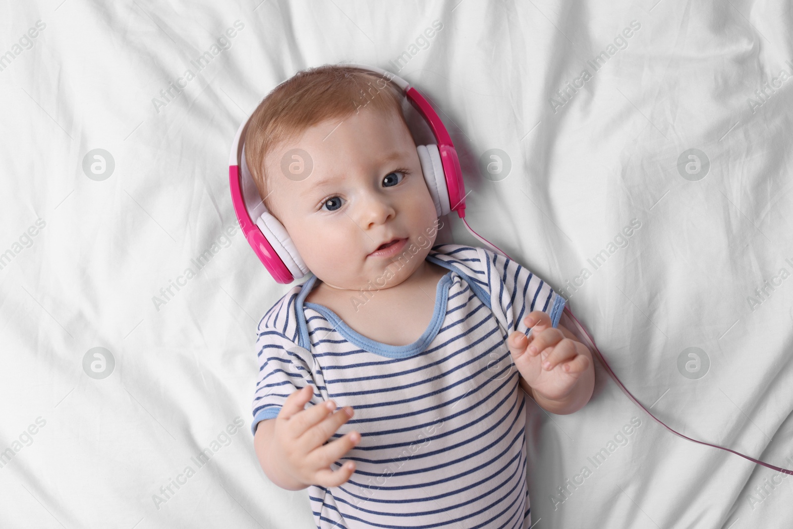 Photo of Cute little baby with headphones lying on bed, top view