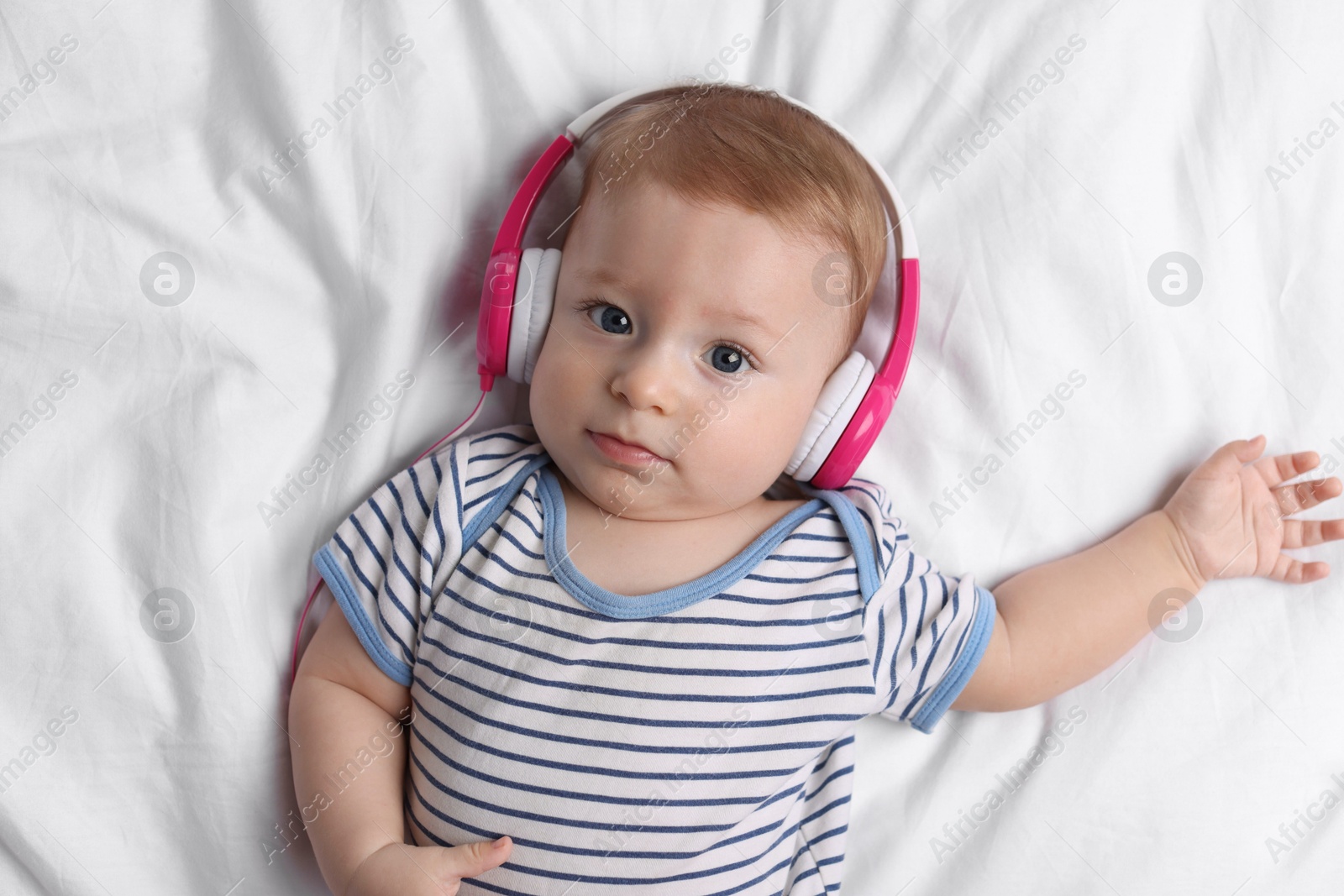 Photo of Cute little baby with headphones lying on bed, top view