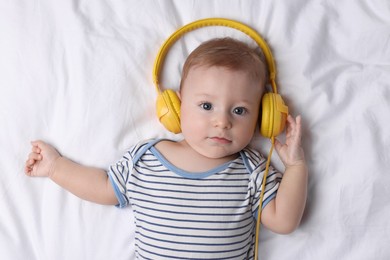 Photo of Cute little baby with headphones lying on bed, top view