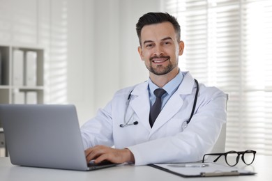 Smiling doctor working with laptop at table in clinic