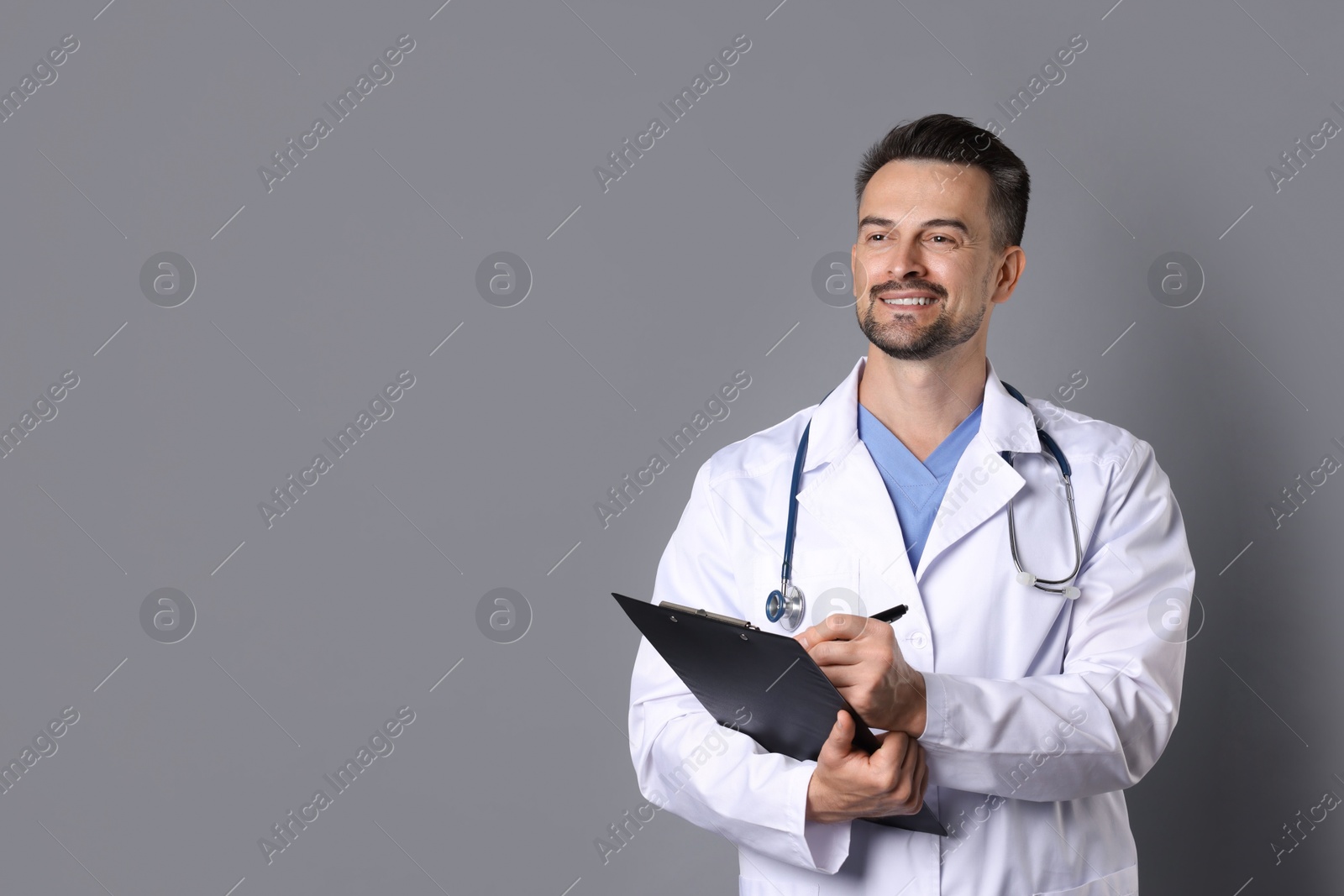 Photo of Smiling doctor with stethoscope and clipboard on grey background, space for text