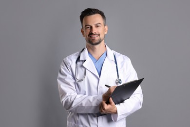 Photo of Smiling doctor with stethoscope and clipboard on grey background