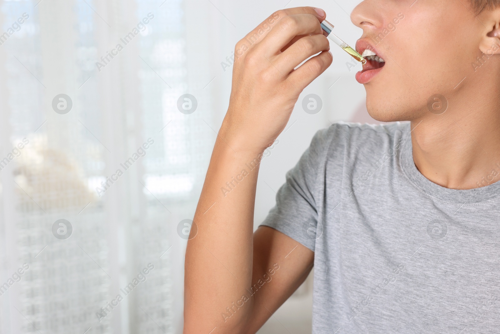 Photo of Young man taking CBD tincture indoors, closeup. Space for text