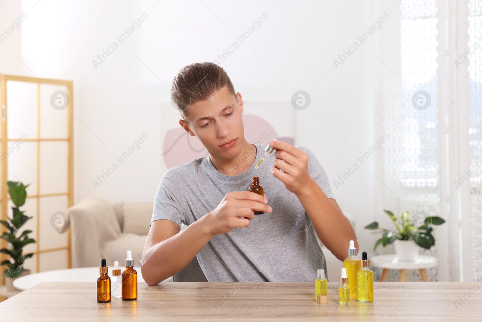 Photo of Young man dripping CBD tincture into bottle from dropper at wooden table