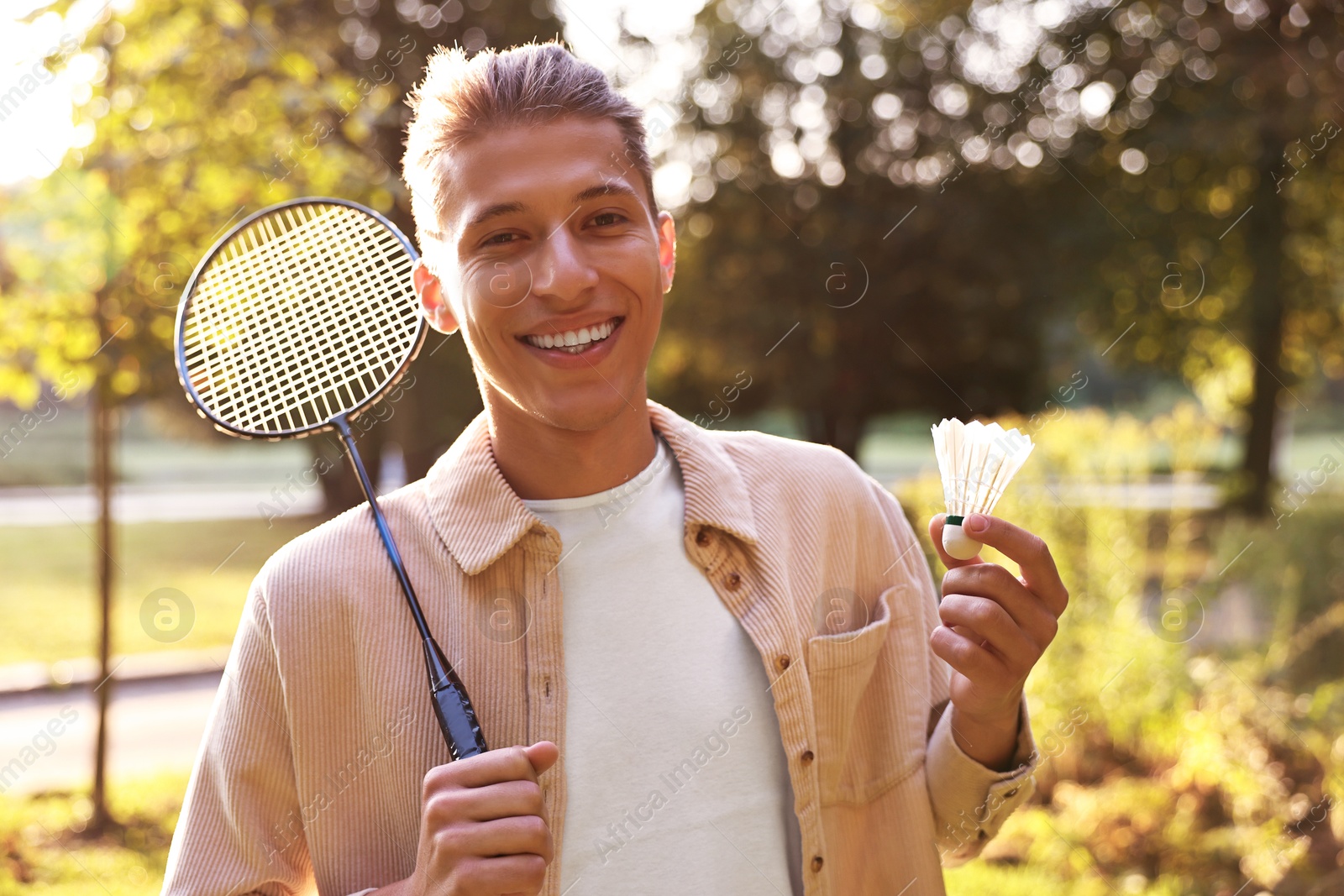 Photo of Happy young man with badminton racket and shuttlecock in park on sunny day