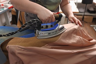 Photo of Young woman with iron working in professional workshop, closeup