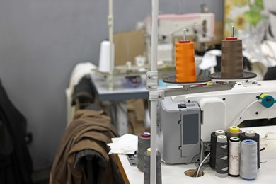 Photo of Sewing machines with spools of thread in professional workshop, closeup