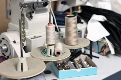 Photo of Sewing machine with spools of thread in professional workshop, closeup