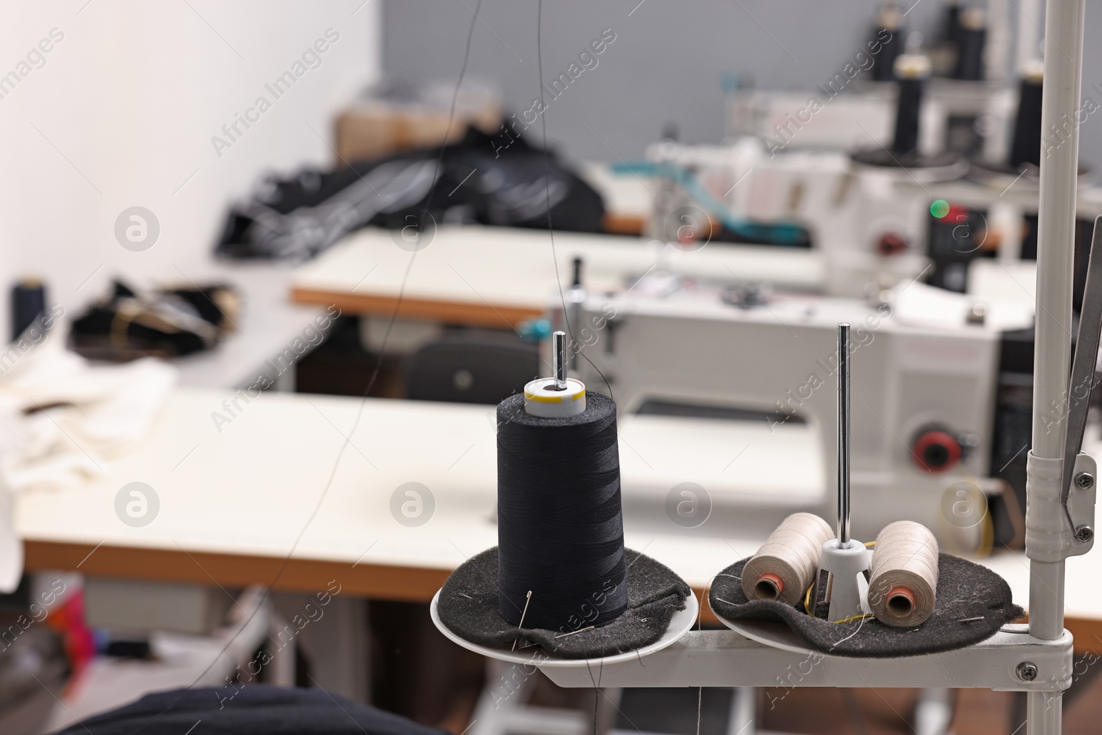 Photo of Sewing machines with spools of thread in professional workshop, closeup