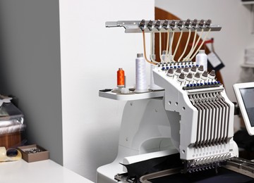 Photo of Sewing machine with spools of thread in professional workshop