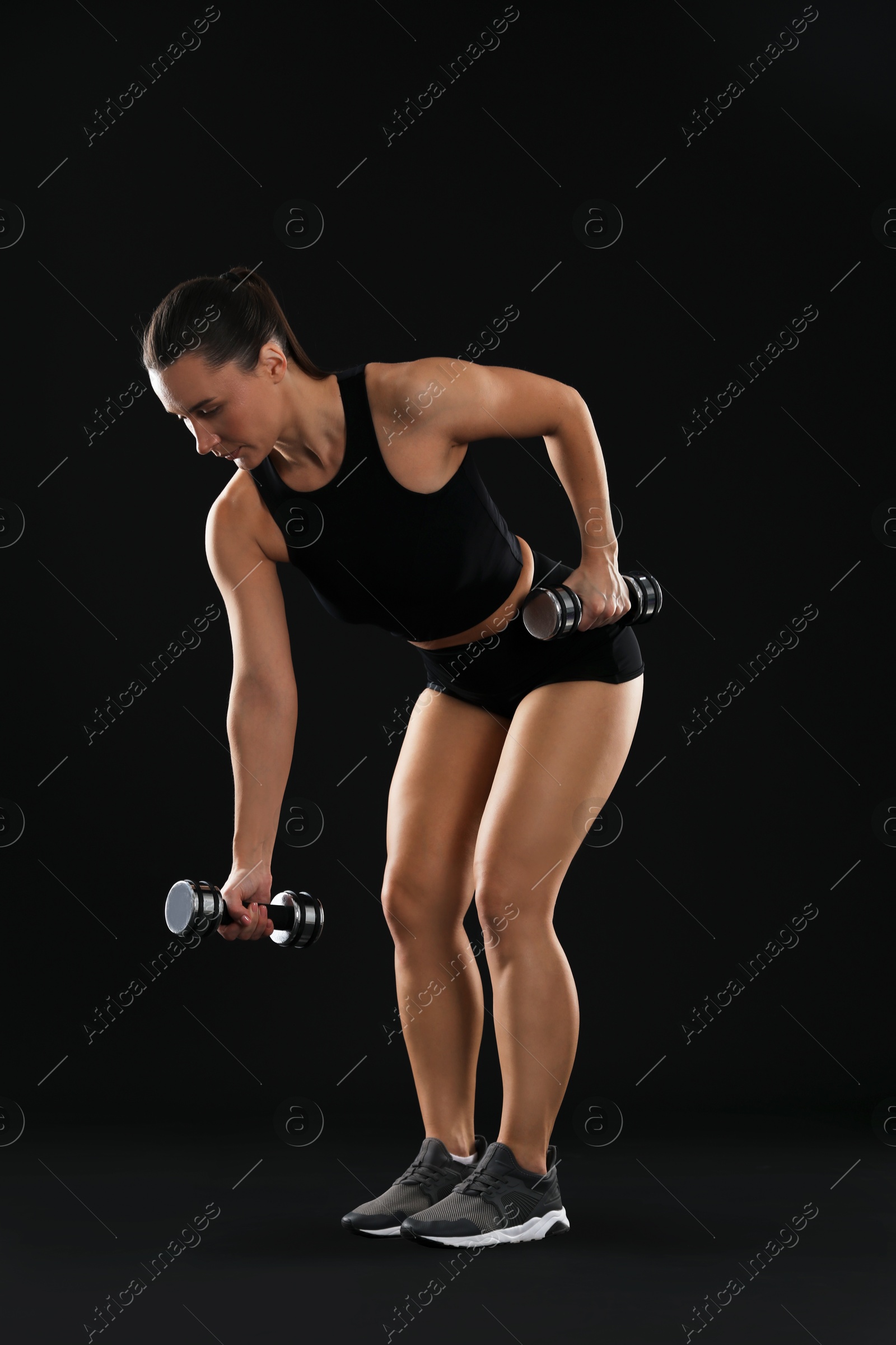 Photo of Woman exercising with dumbbells on black background