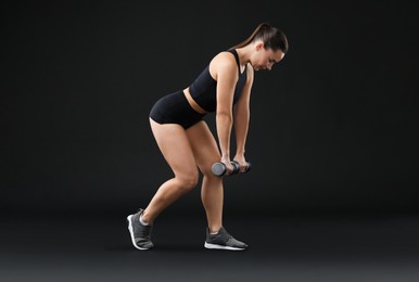 Woman exercising with dumbbells on black background