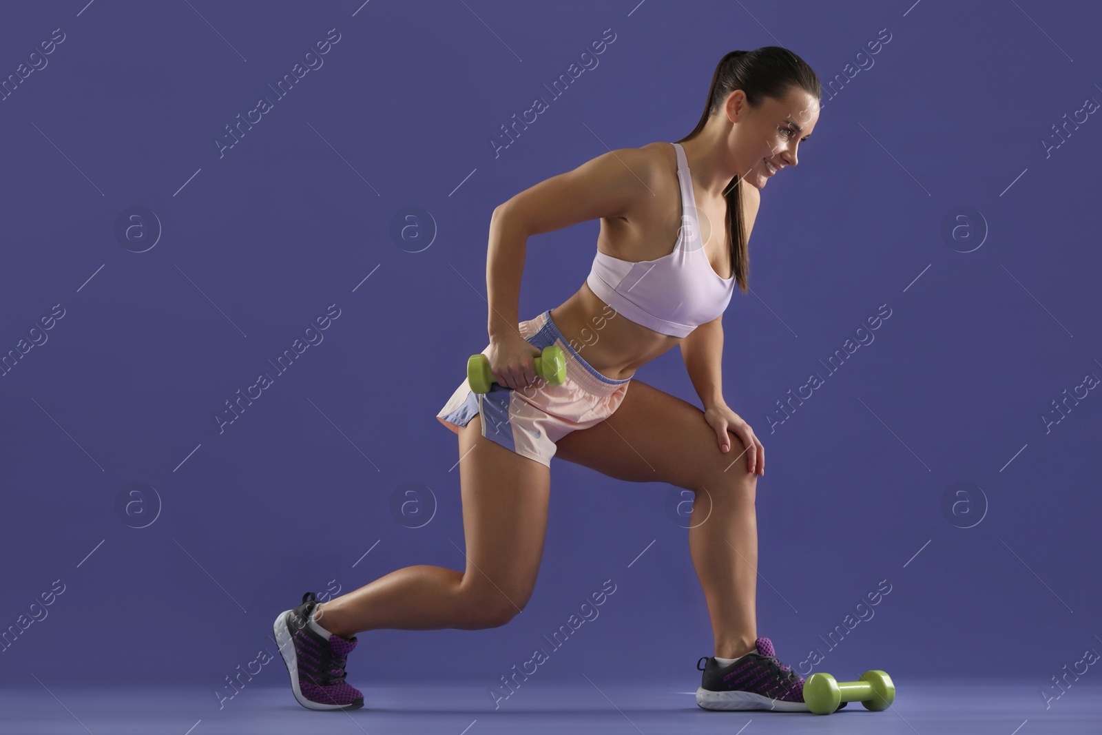 Photo of Woman exercising with dumbbells on purple background