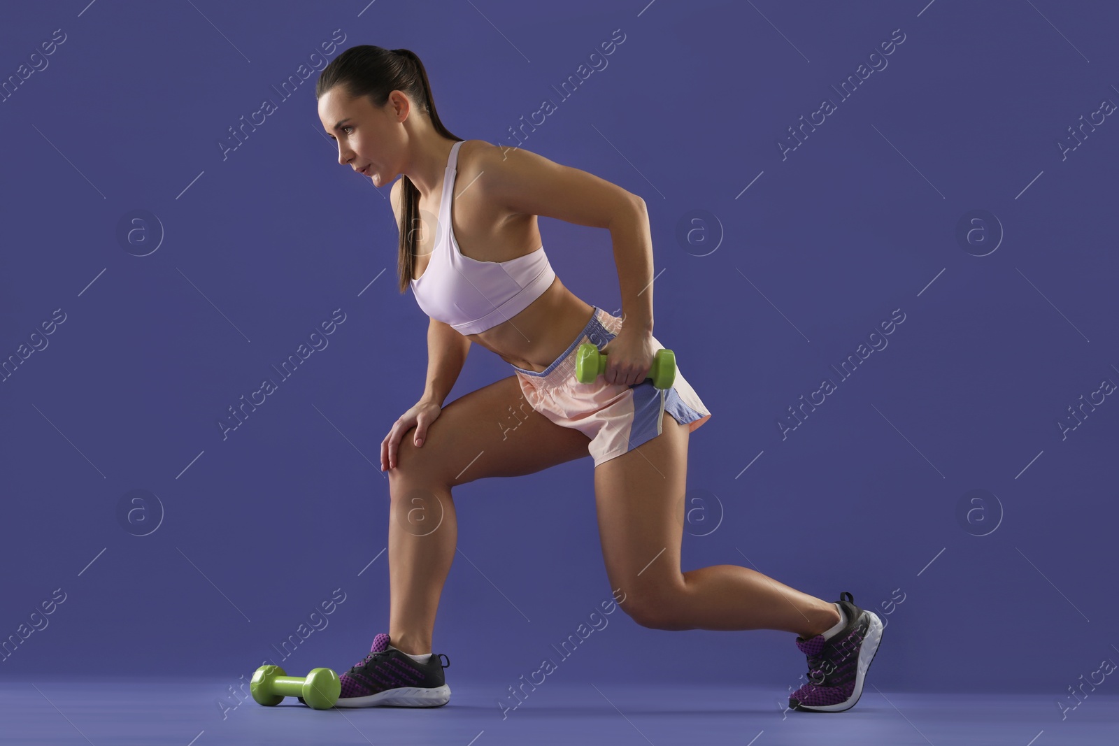 Photo of Woman exercising with dumbbells on purple background