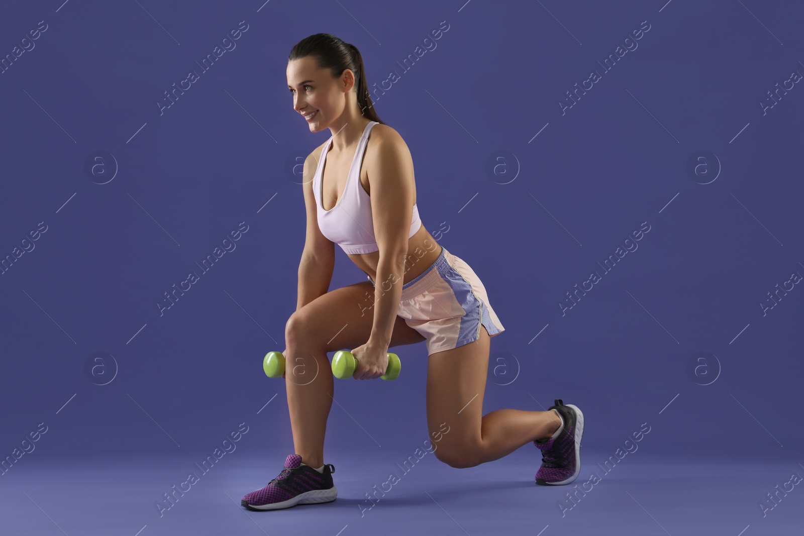 Photo of Woman exercising with dumbbells on purple background