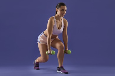 Photo of Woman exercising with dumbbells on purple background