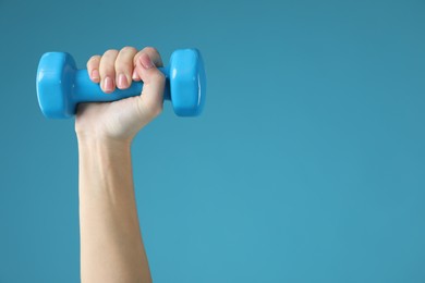 Photo of Woman exercising with dumbbell on light blue background, closeup. Space for text