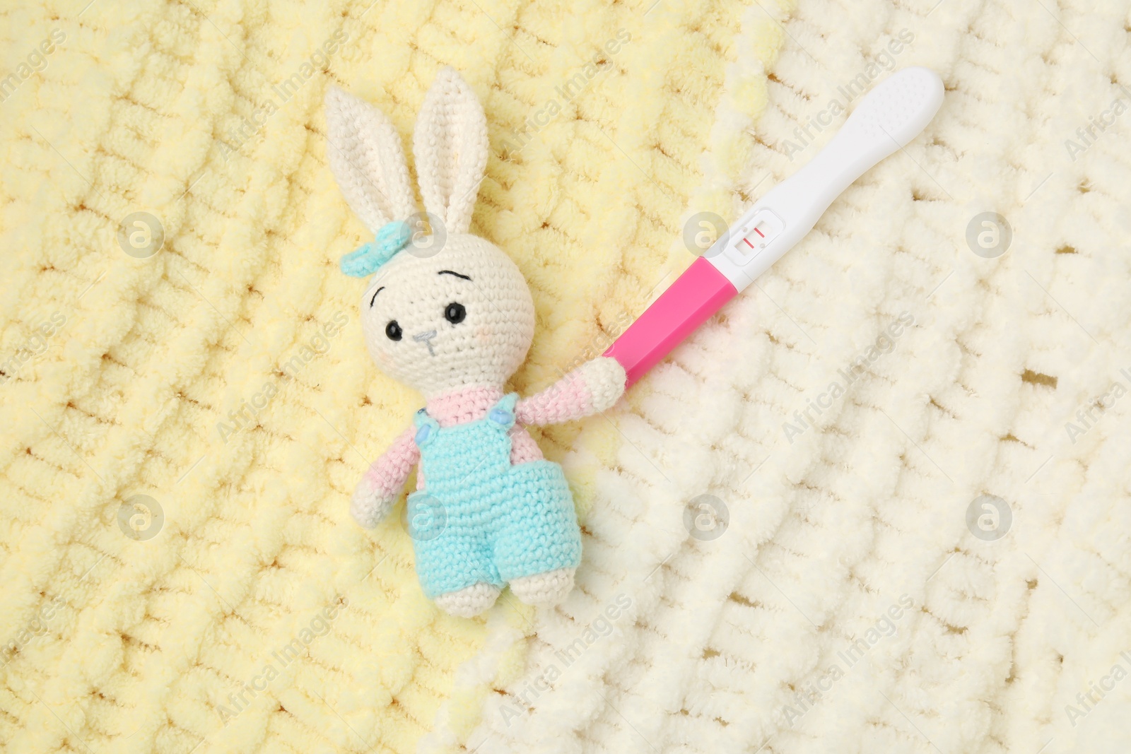 Photo of Pregnancy test and bunny toy on yellow knitted fabric, top view