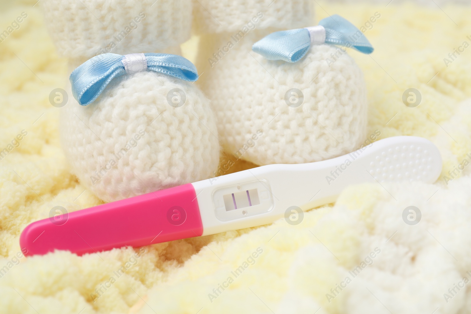 Photo of Pregnancy test and baby shoes on yellow knitted fabric, closeup