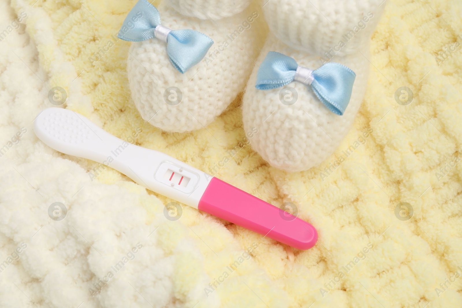 Photo of Pregnancy test and baby shoes on yellow knitted fabric, closeup