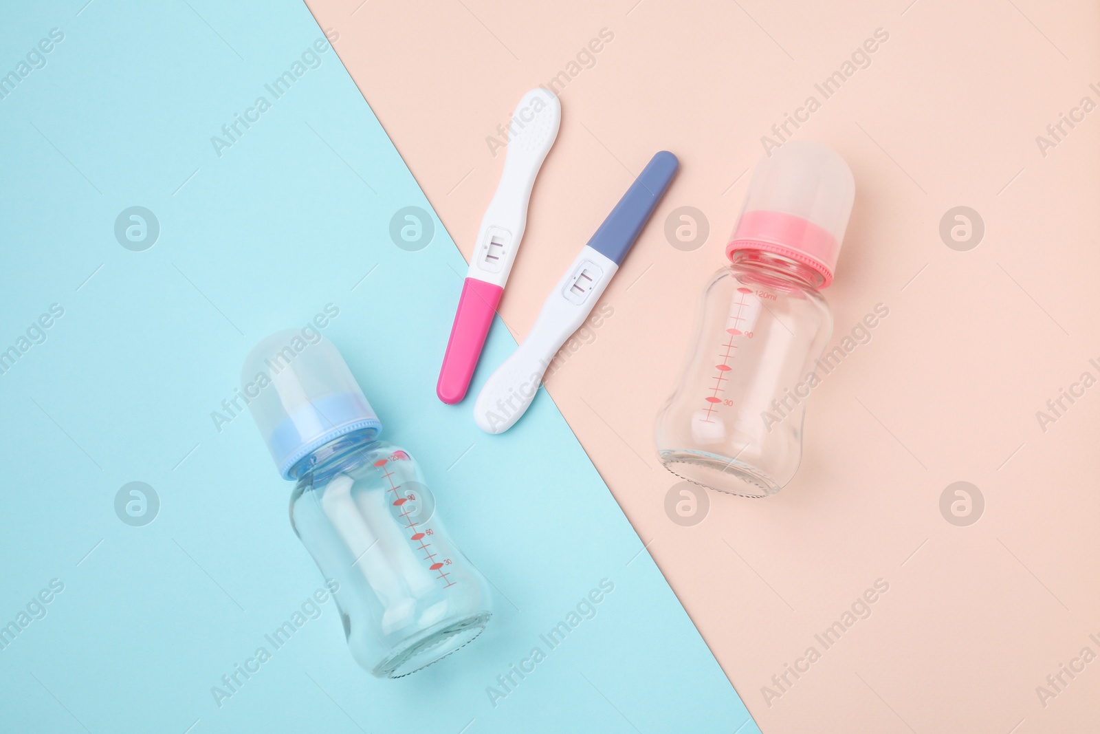 Photo of Two pregnancy tests and baby bottles on color background, flat lay