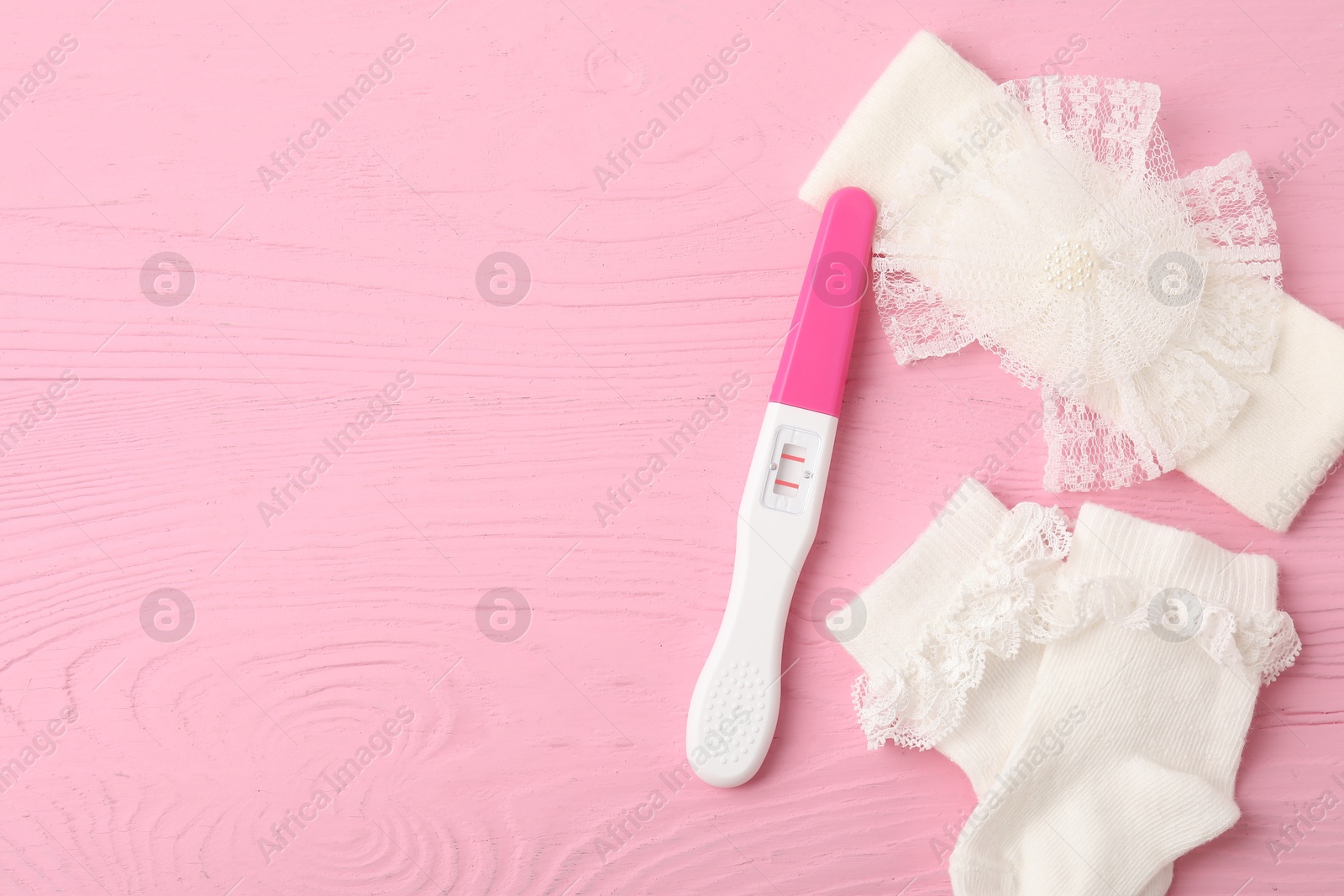 Photo of Pregnancy test and baby socks on pink wooden table, flat lay. Space for text