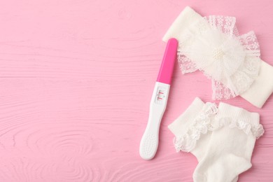 Pregnancy test and baby socks on pink wooden table, flat lay. Space for text