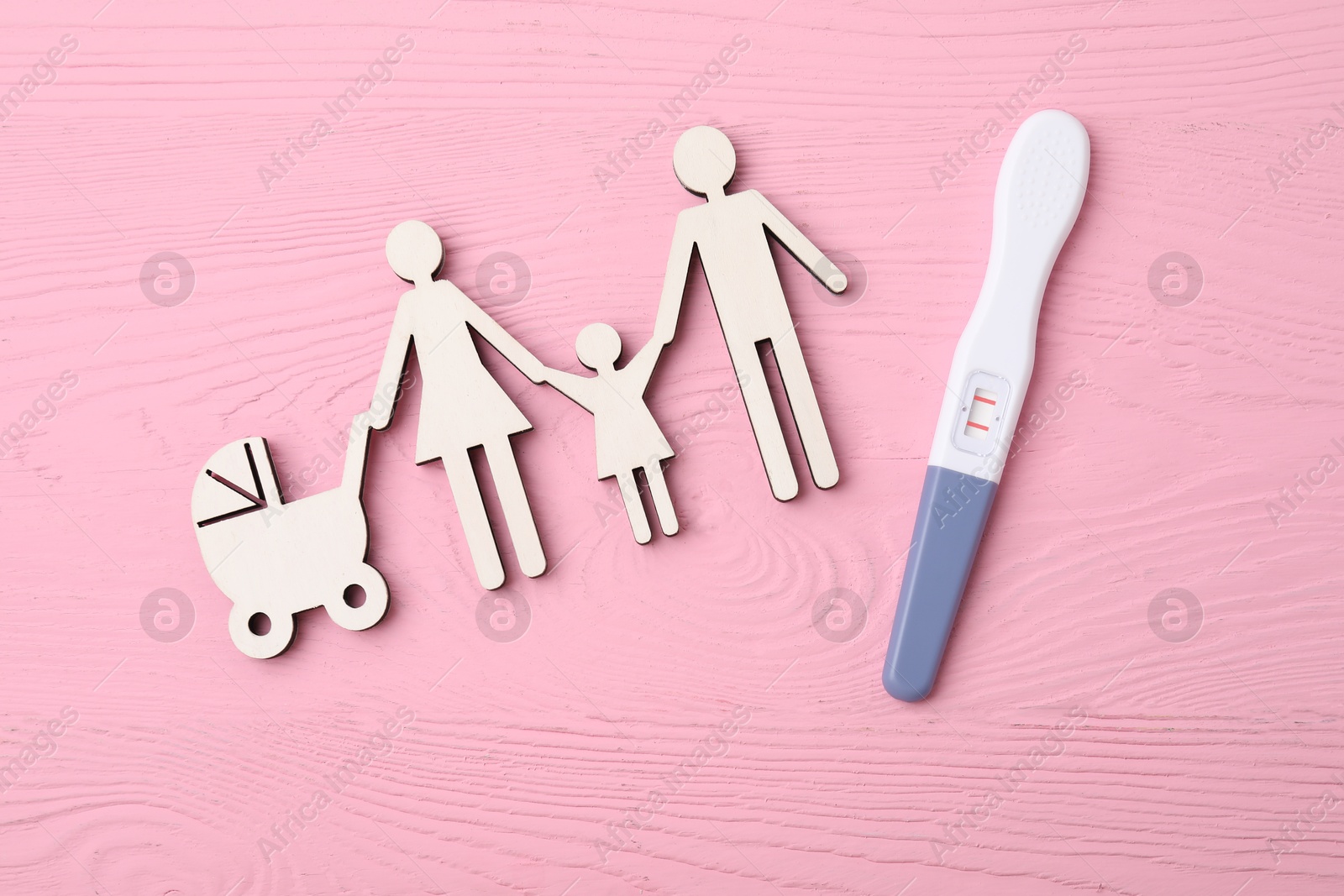 Photo of Pregnancy test and cutout of family on pink wooden table, top view