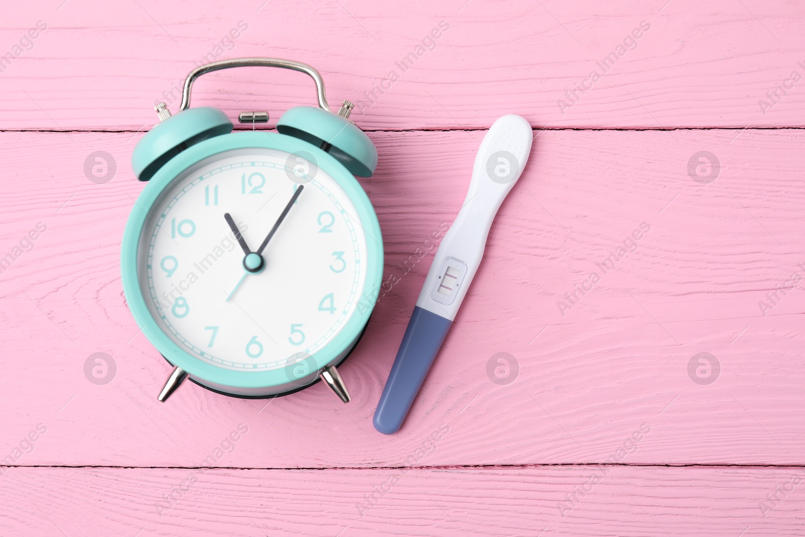 Photo of Pregnancy test and alarm clock on pink wooden table, top view. Space for text