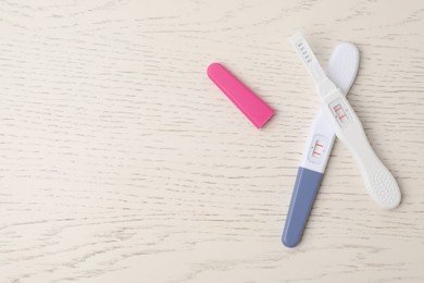 Two pregnancy tests on white wooden table, top view. Space for text