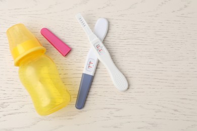 Photo of Two pregnancy tests and baby bottle on white wooden table, flat lay. Space for text