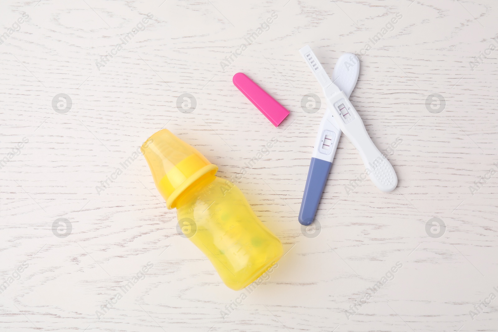 Photo of Two pregnancy tests and baby bottle on white wooden table, flat lay