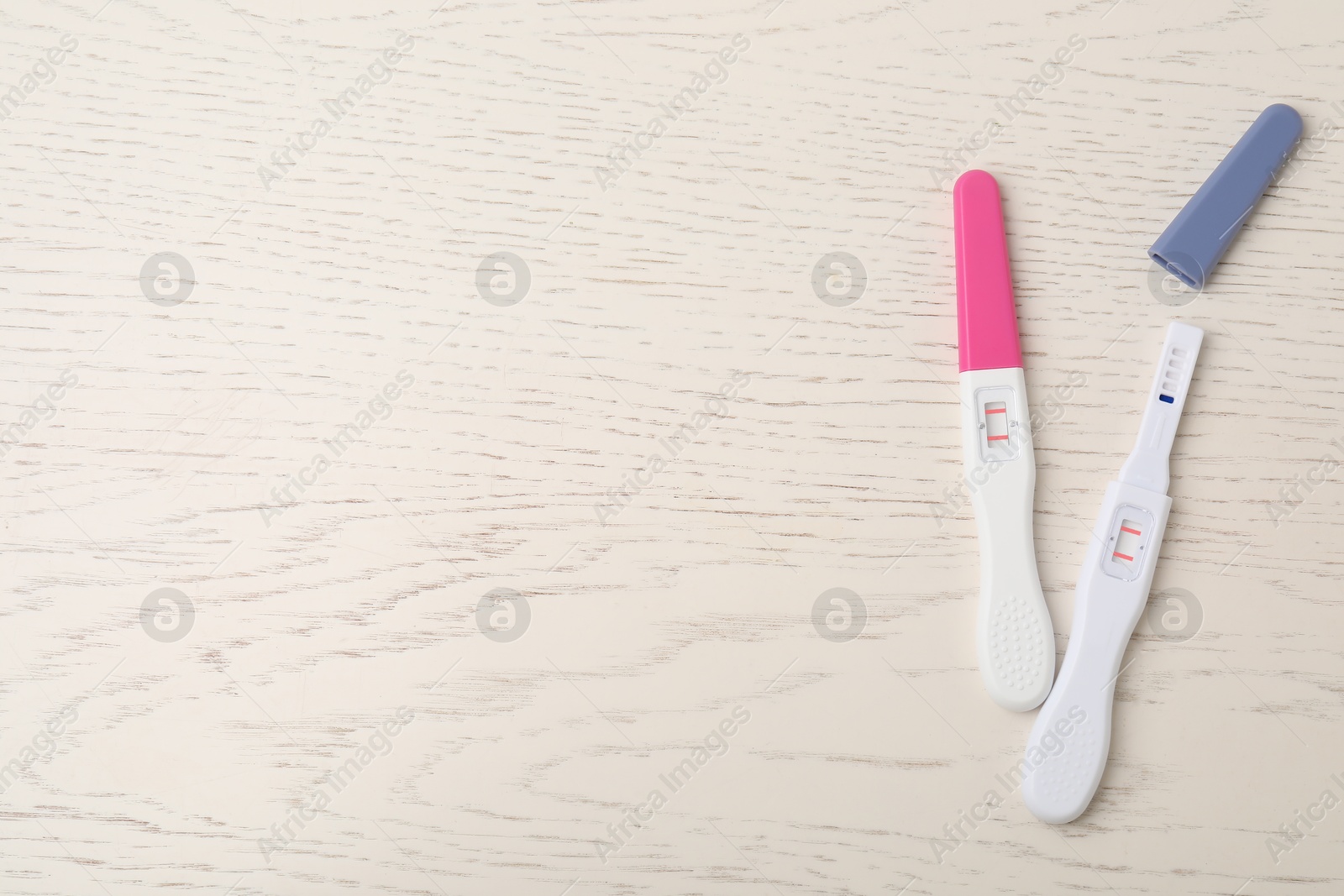 Photo of Two pregnancy tests on white wooden table, top view. Space for text