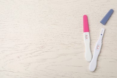 Photo of Two pregnancy tests on white wooden table, top view. Space for text