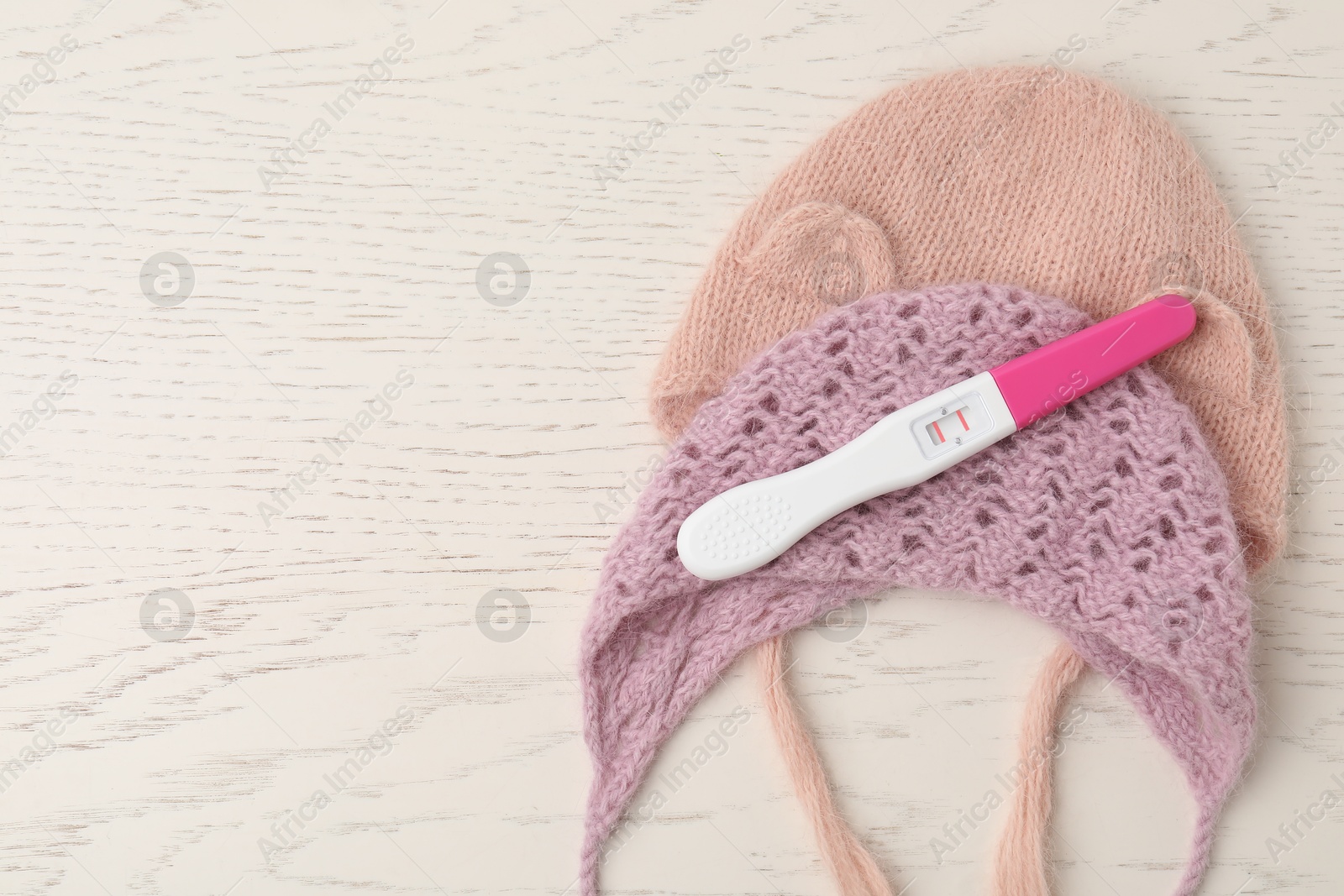 Photo of Pregnancy test and baby hats on white wooden table, flat lay. Space for text