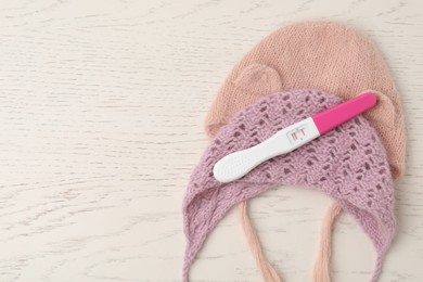 Photo of Pregnancy test and baby hats on white wooden table, flat lay. Space for text