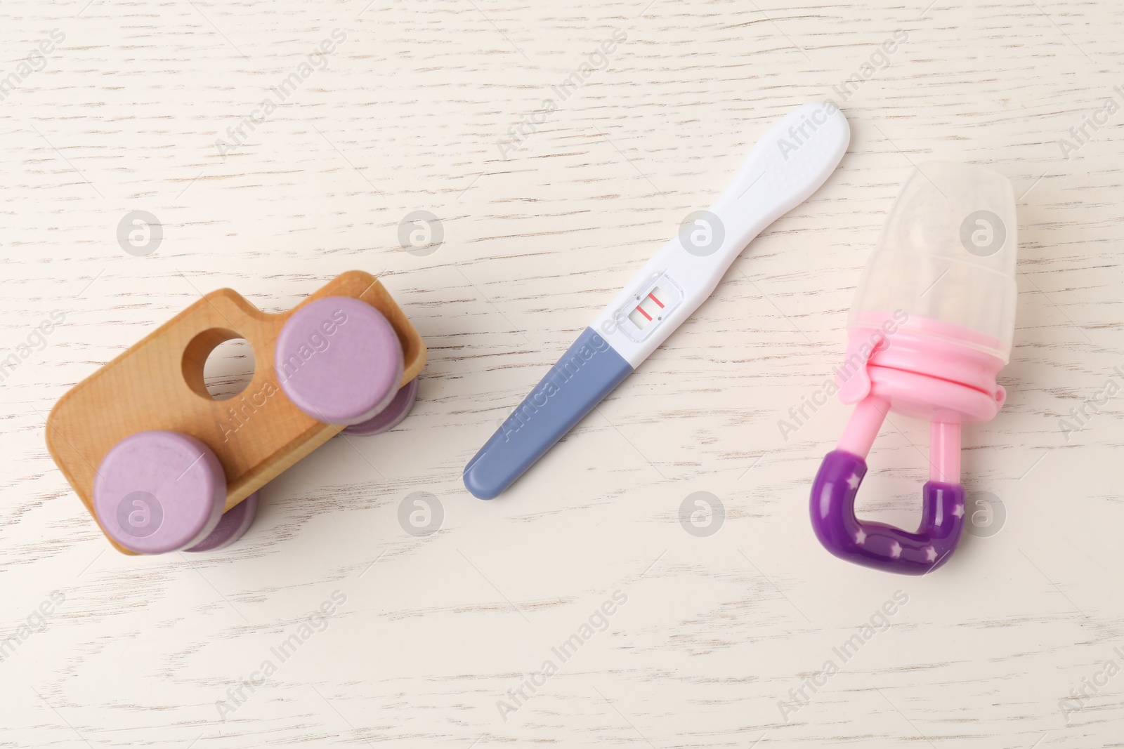 Photo of Pregnancy test and baby toys on white wooden table, flat lay