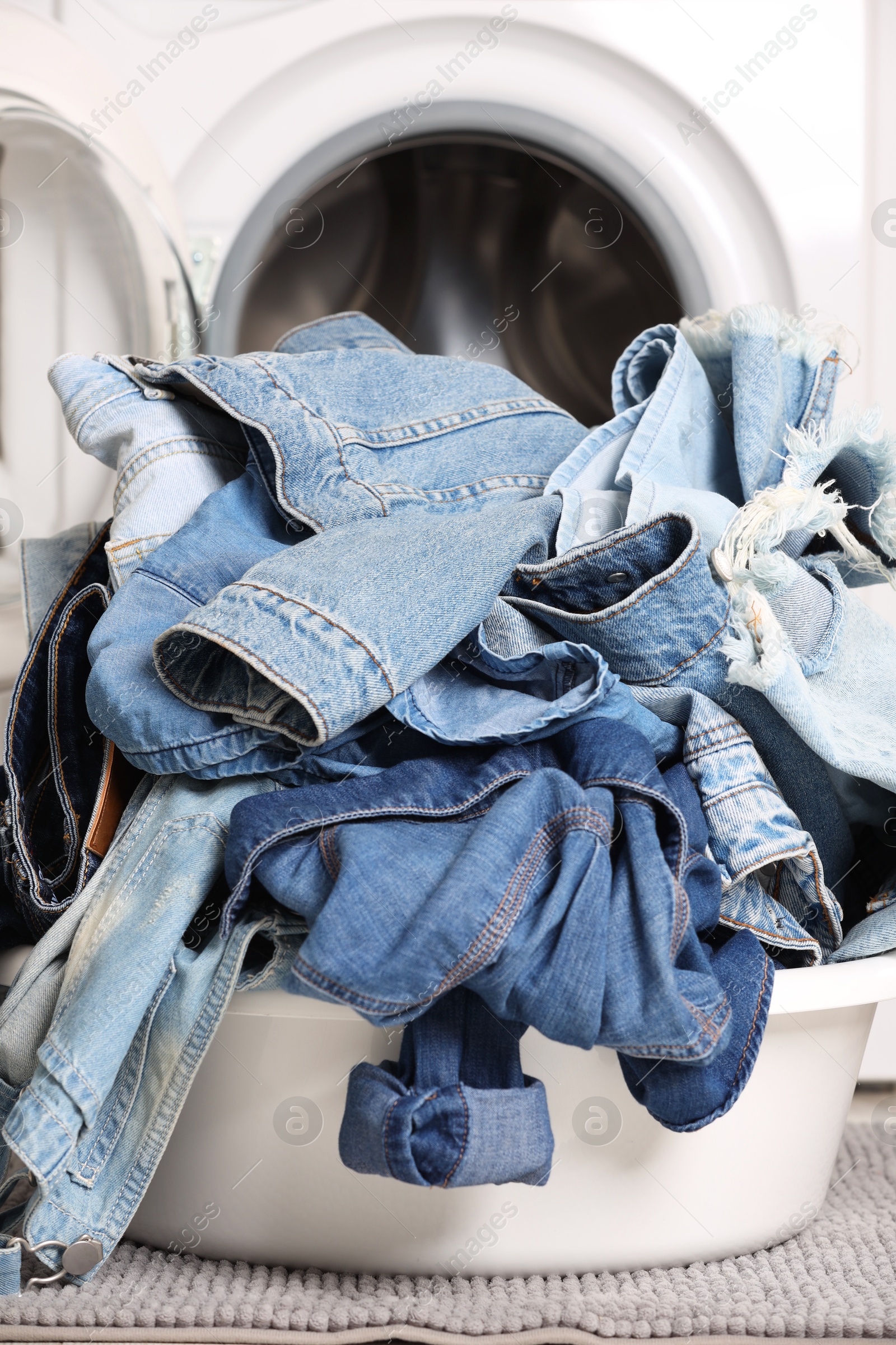 Photo of Washing machine and laundry basket with dirty denim clothes indoors