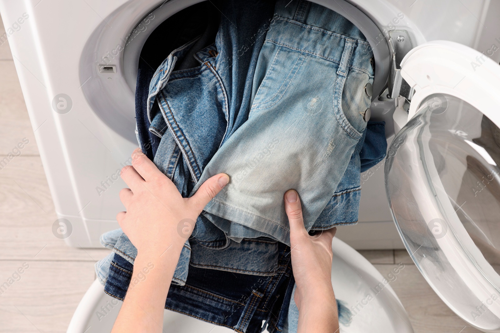 Photo of Woman putting dirty jeans and other denim clothes into washing machine, closeup