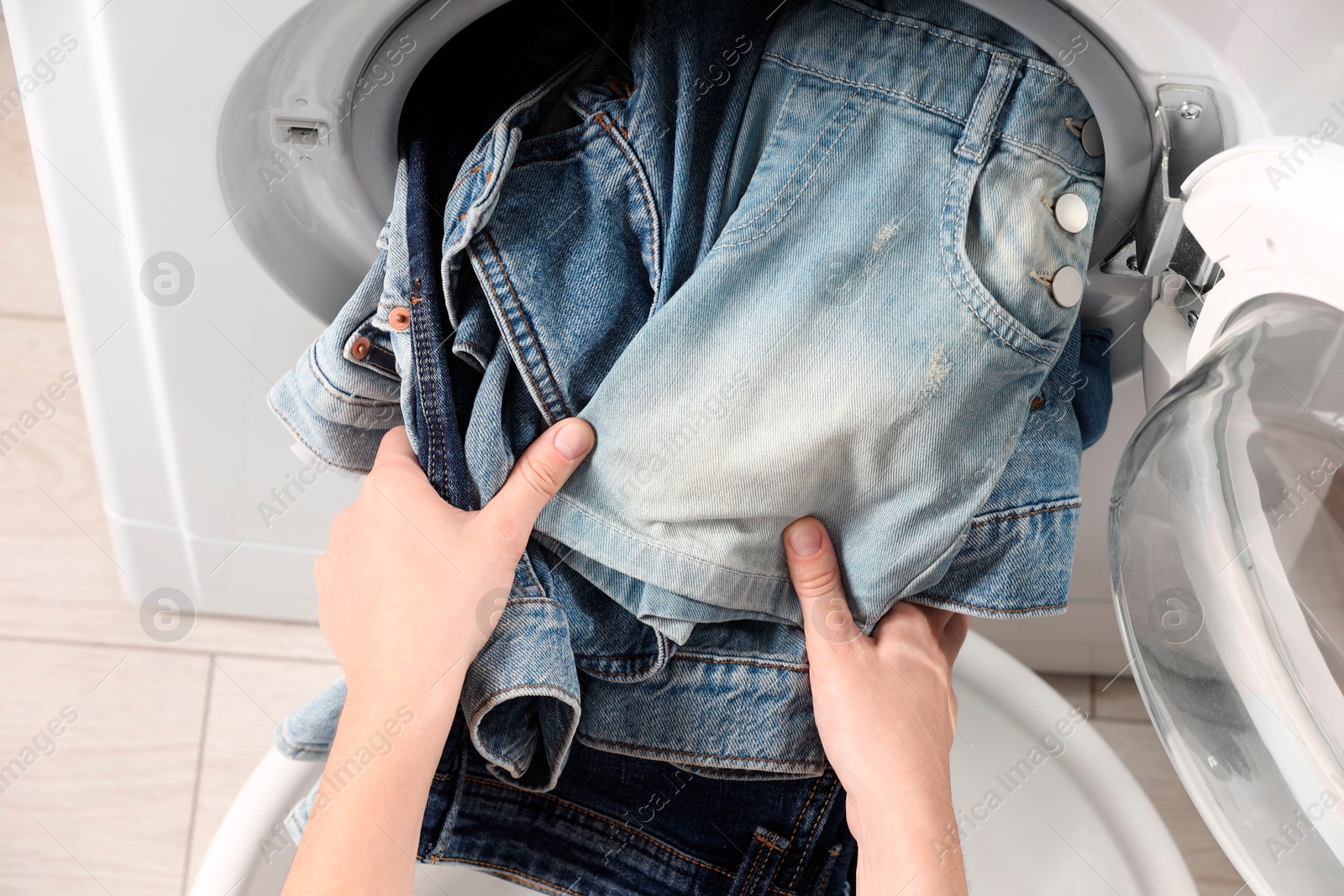 Photo of Woman putting dirty jeans and other denim clothes into washing machine, closeup