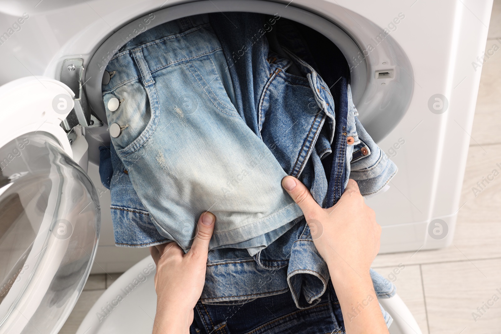 Photo of Woman putting dirty jeans and other denim clothes into washing machine, closeup