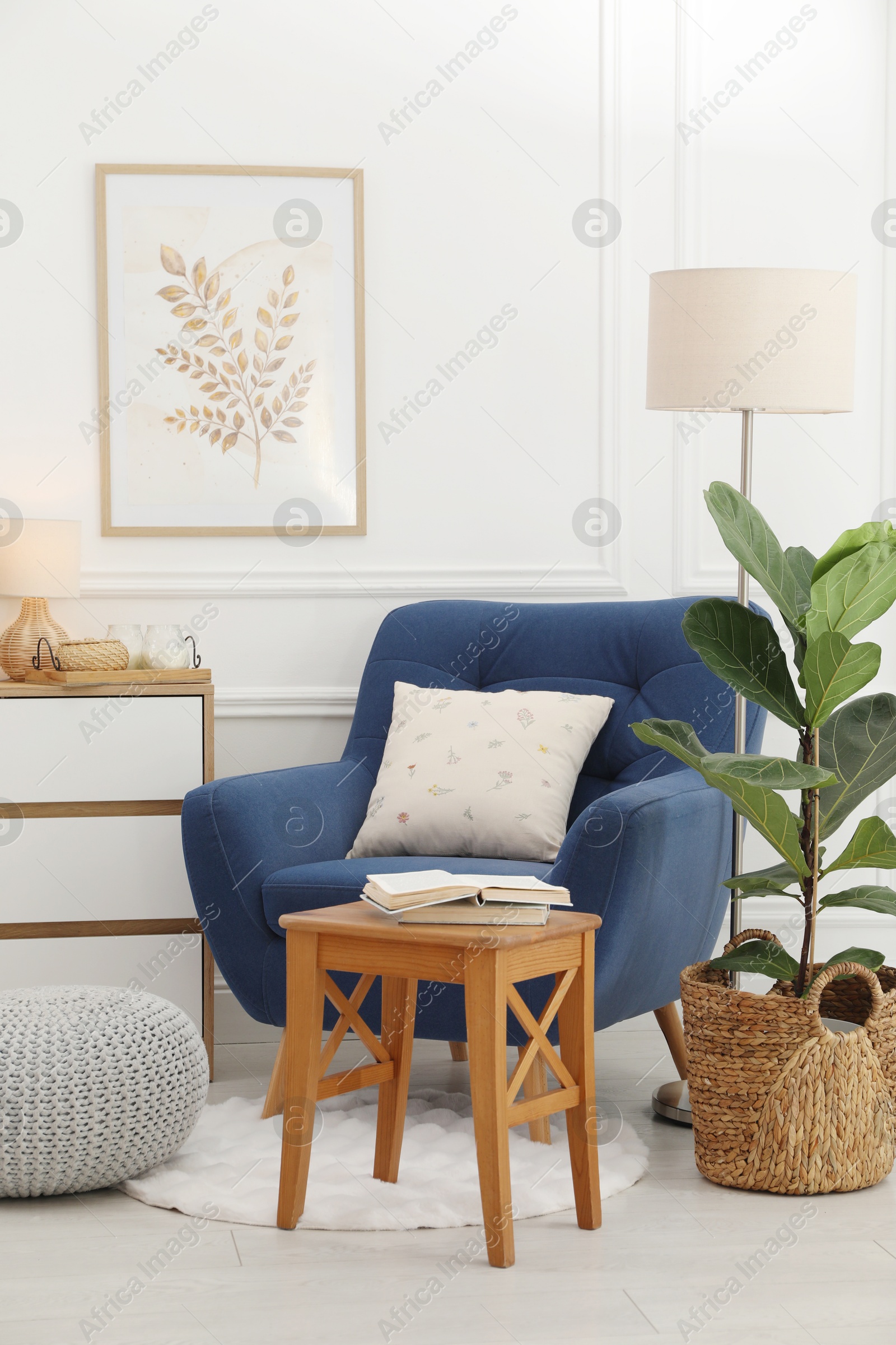 Photo of Stool, books, armchair and houseplant in room. Interior design