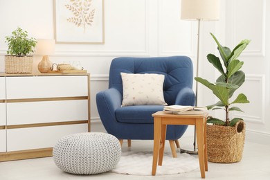 Photo of Stool, books, armchair and houseplants in room. Interior design