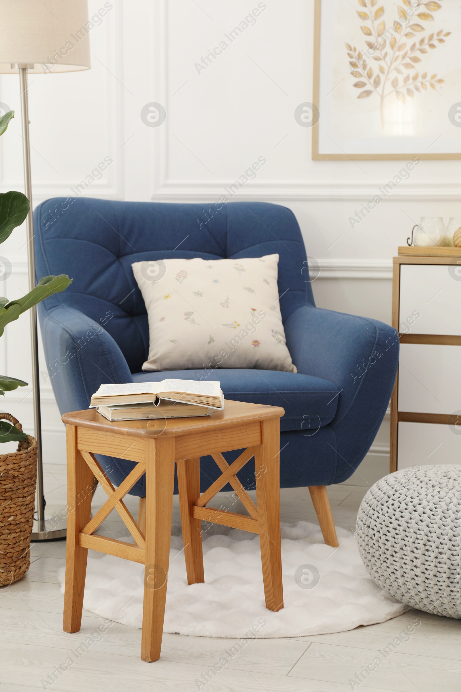 Photo of Stool, books, armchair and houseplant in room. Interior design